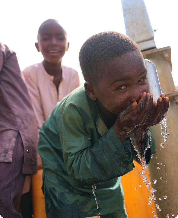 A young Nigerian boy smiling as he drinks fresh water from his hands at a newly installed community borehole water station.