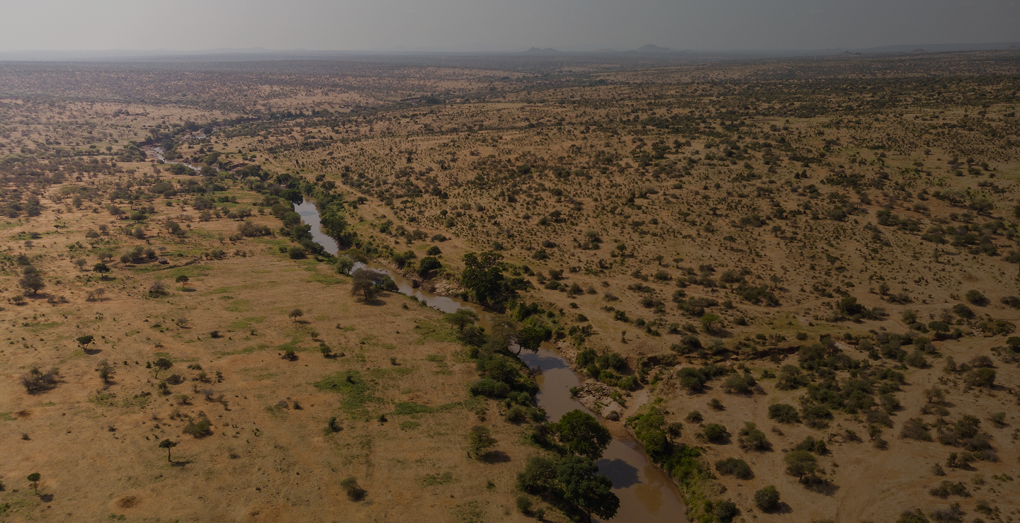 High-angle aerial shot of a brown river winding through a dry, arid savanna landscape dotted with scattered trees and low vegetation.