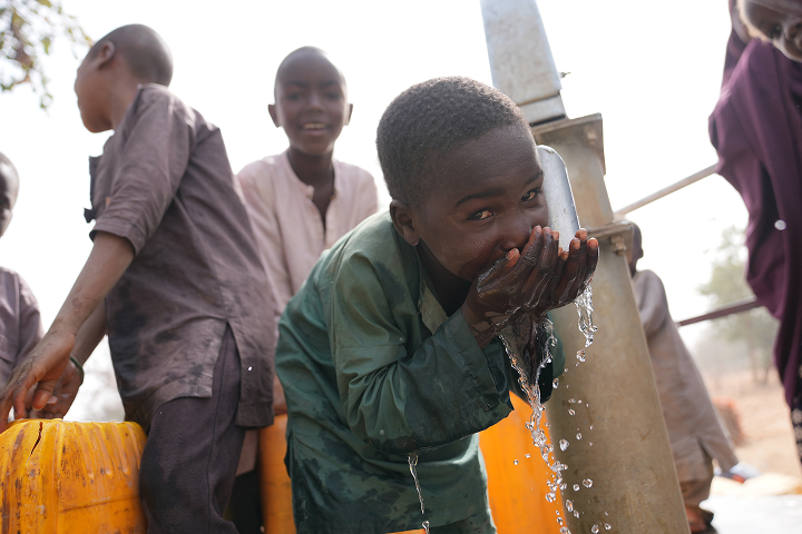 A young Nigerian boy smiling as he drinks fresh water from his hands at a newly installed community borehole water station.