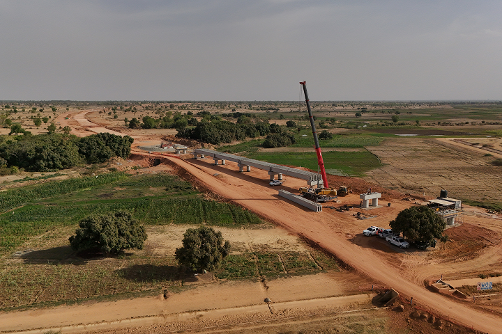 High-angle aerial shot of a concrete railway viaduct under construction stretching across open rural fields, with a red mobile crane stationed on site.