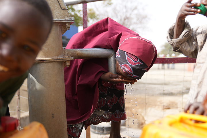 Close-up of a girl wearing a red hijab drinking fresh water directly from her cupped hands at a clean community water pump.