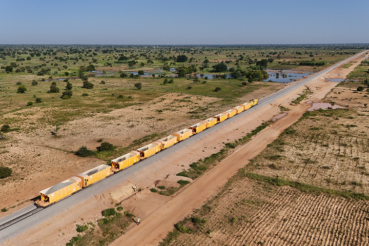 High-angle drone view of a long yellow ballast hopper train standing on a newly laid railway track running through a rural landscape.