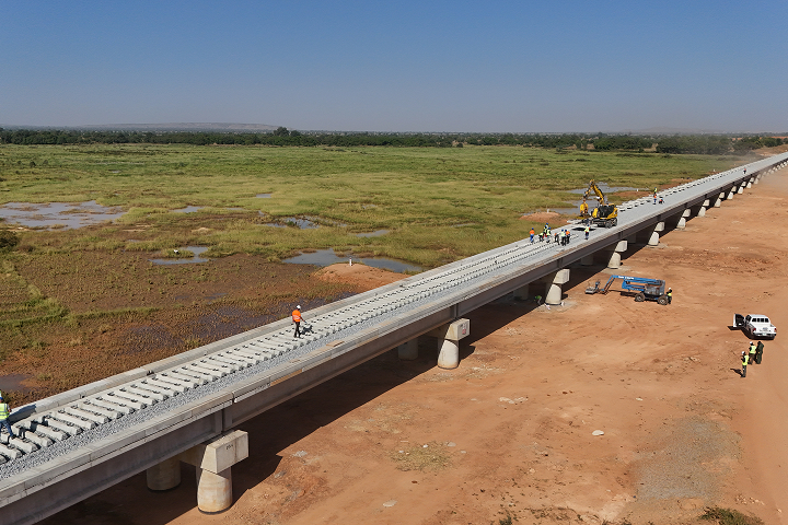 Elevated drone view of an extensive concrete railway bridge with precast concrete sleepers installed along the deck, running parallel to wetland terrain.