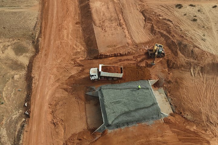 Top-down aerial view of a construction site showing a tipper truck unloading soil near a newly built concrete culvert structure.