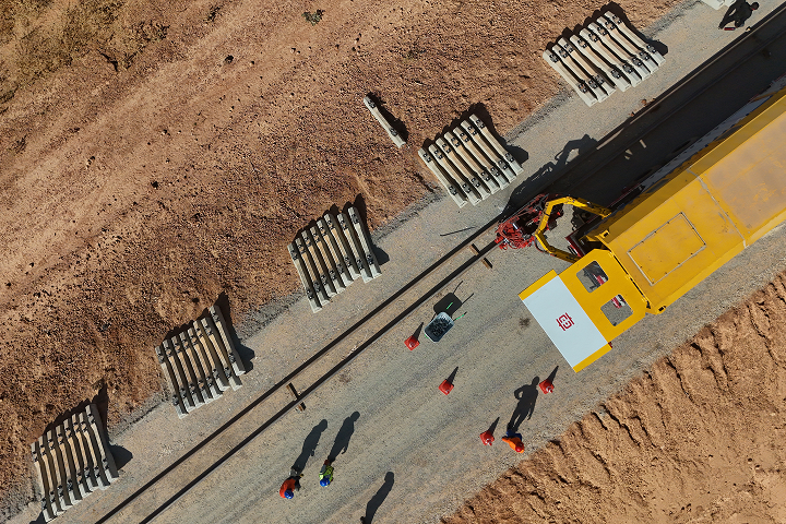 Direct overhead aerial view showing railway track installation with precast concrete sleepers laid out alongside a yellow track-laying machine.
